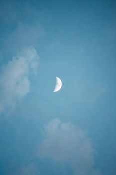 A serene crescent moon amidst a soft blue sky and gentle clouds.