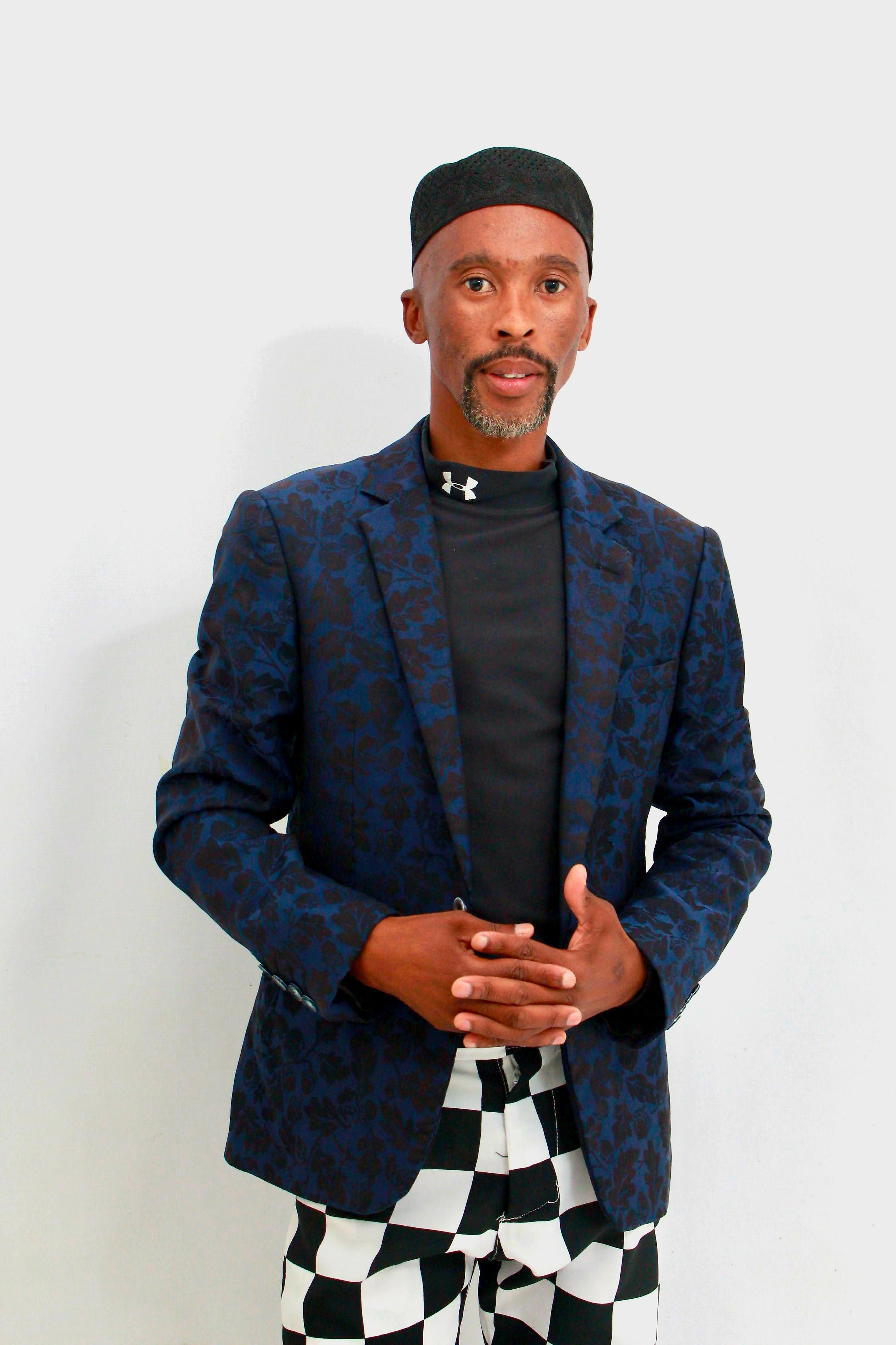 A fashionable man poses confidently in bold patterned attire against a white backdrop.