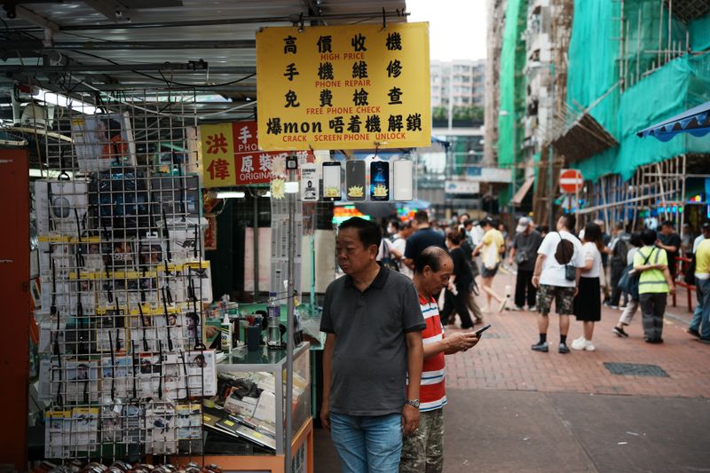 Lively street scene showcasing a phone repair shop and people walking by in an urban market environment.
