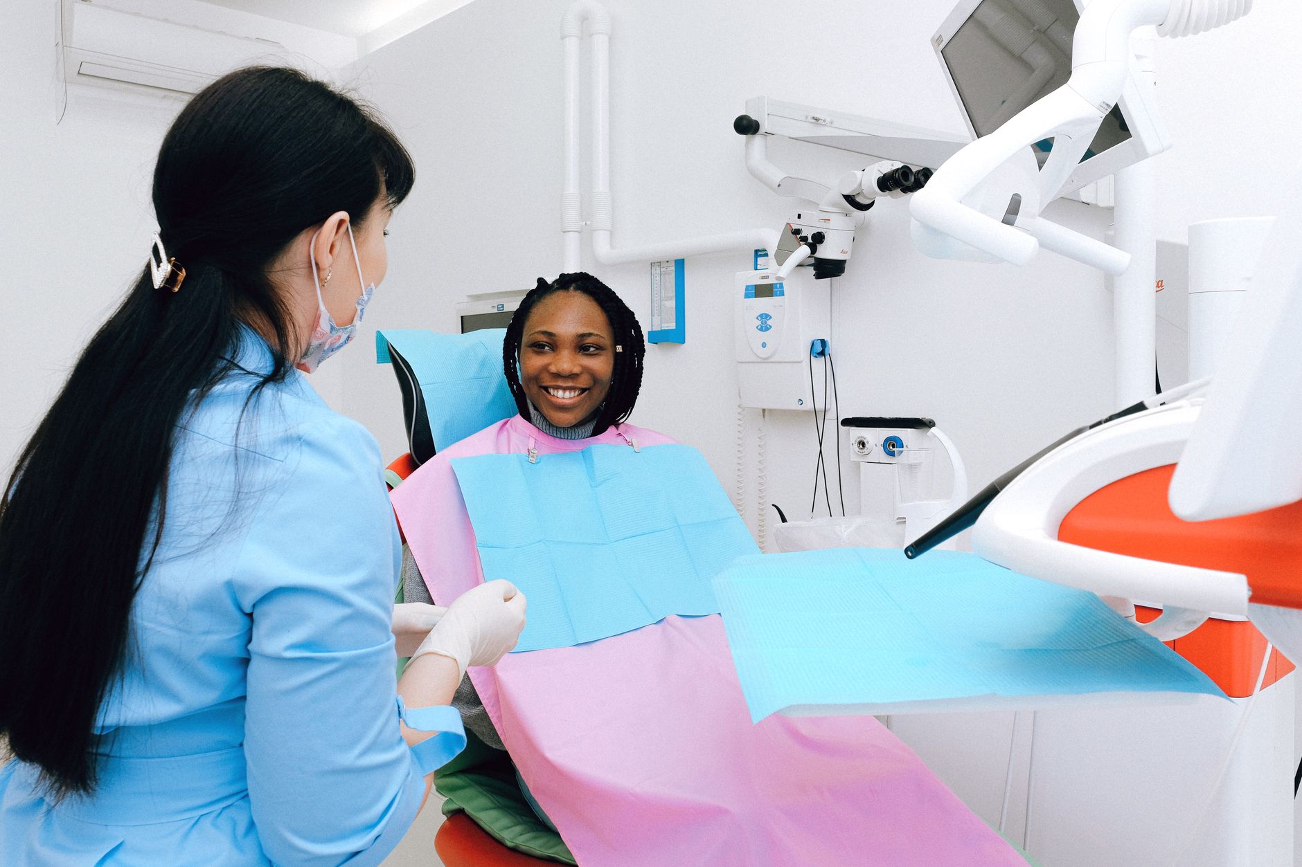 A patient in a dental chair looking at her smile in a hand mirror while discussing veneers, bonding, and Invisalign options with her dentist in Bloor West Village, Toronto