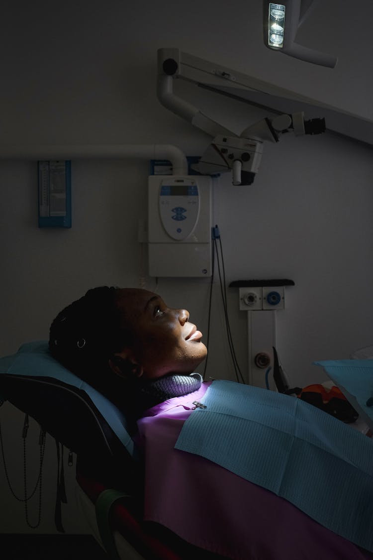 Ethnic Female Patient Sitting In Dental Chair In Dark Room