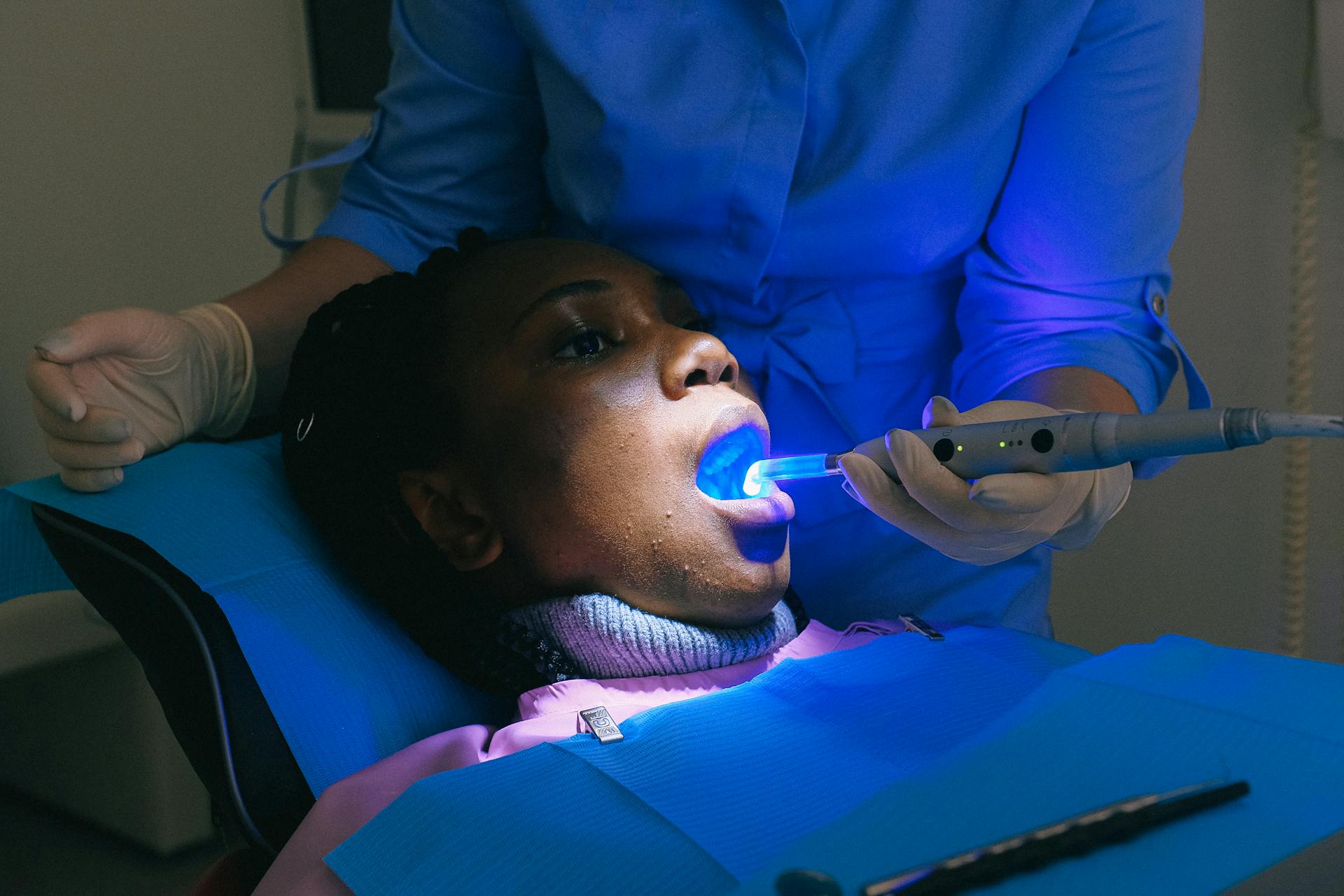 African American woman sitting in dental chair and receiving treatment with curing light from crop doctor