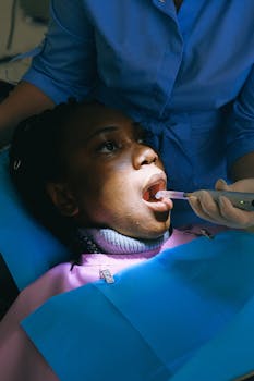 A woman undergoing dental treatment with curing light in a clinical setting.