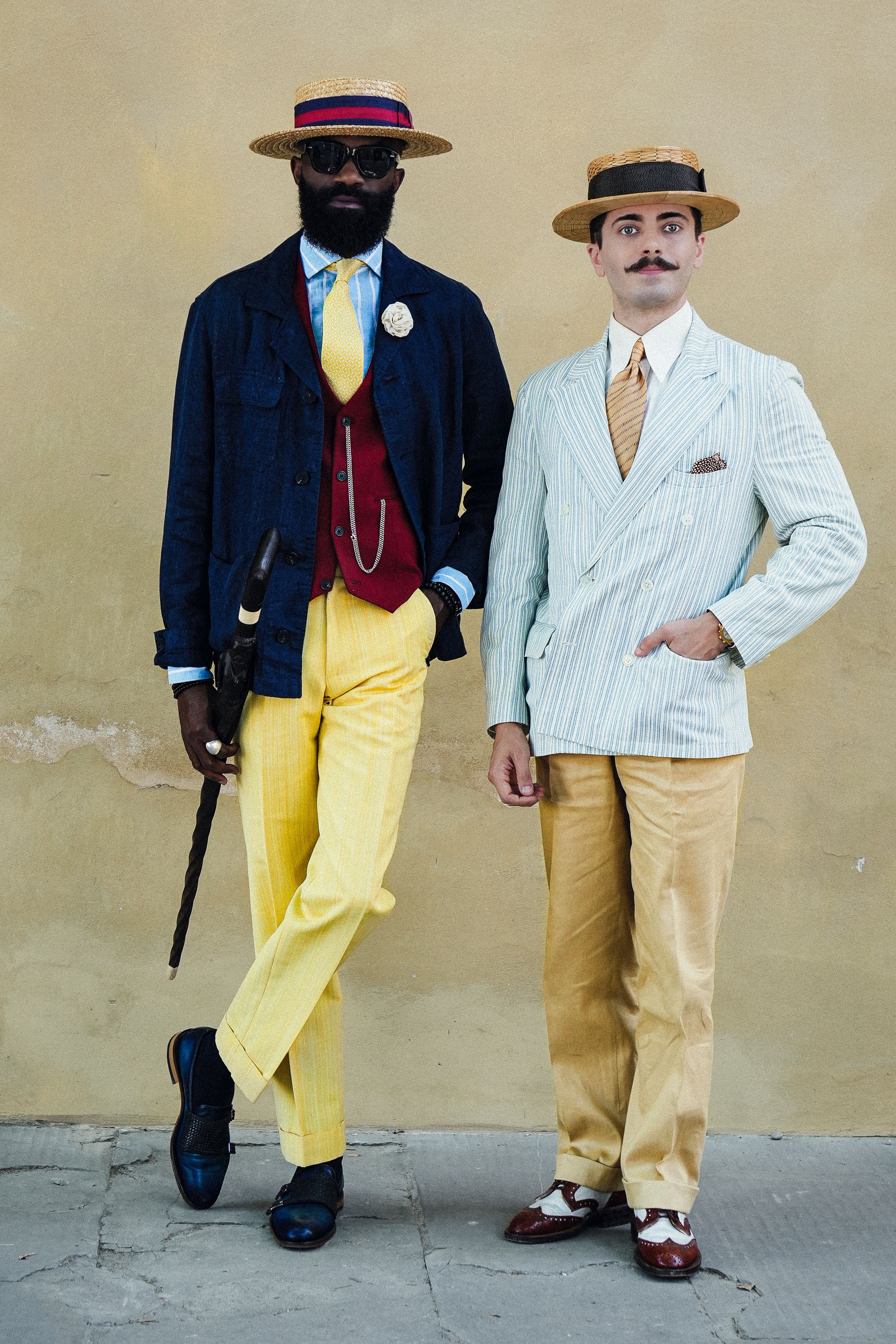 Two men in vintage attire pose against a rustic wall in Florence.