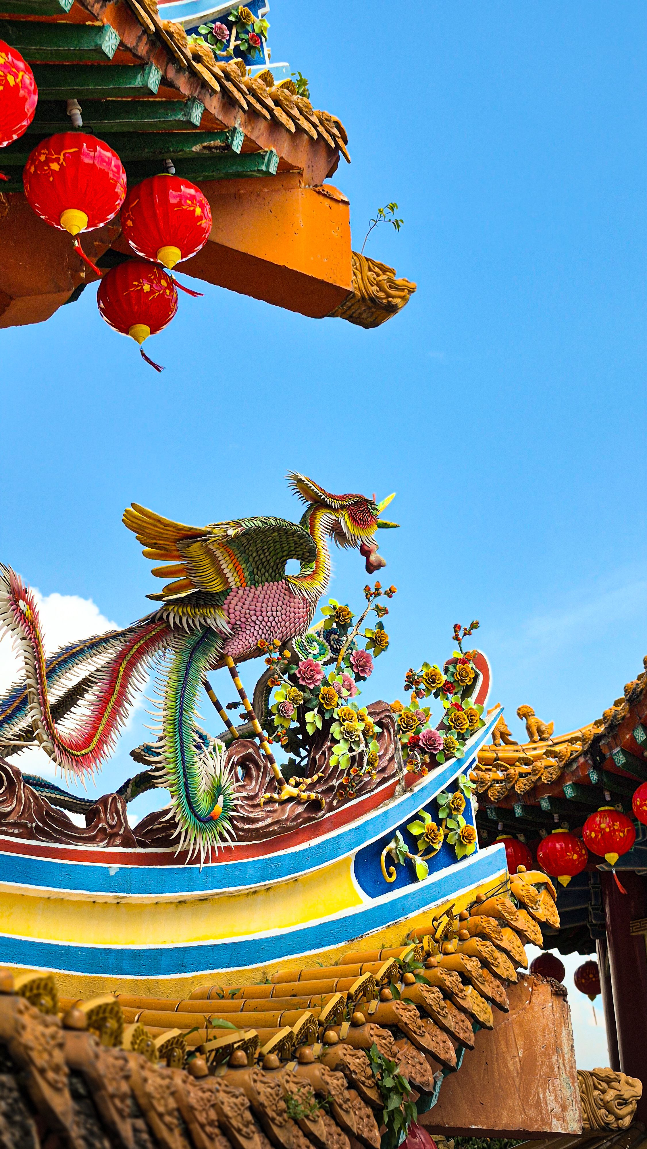 Colorful dragon sculpture on a traditional Chinese temple roof under a clear blue sky.