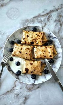 A mouth-watering plate of blueberry-filled pancakes served with yogurt on a marble table.