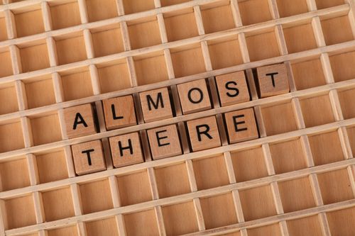 Free Wooden letter tiles spelling 'Almost There' on a wooden grid, conveying progress and motivation. Stock Photo