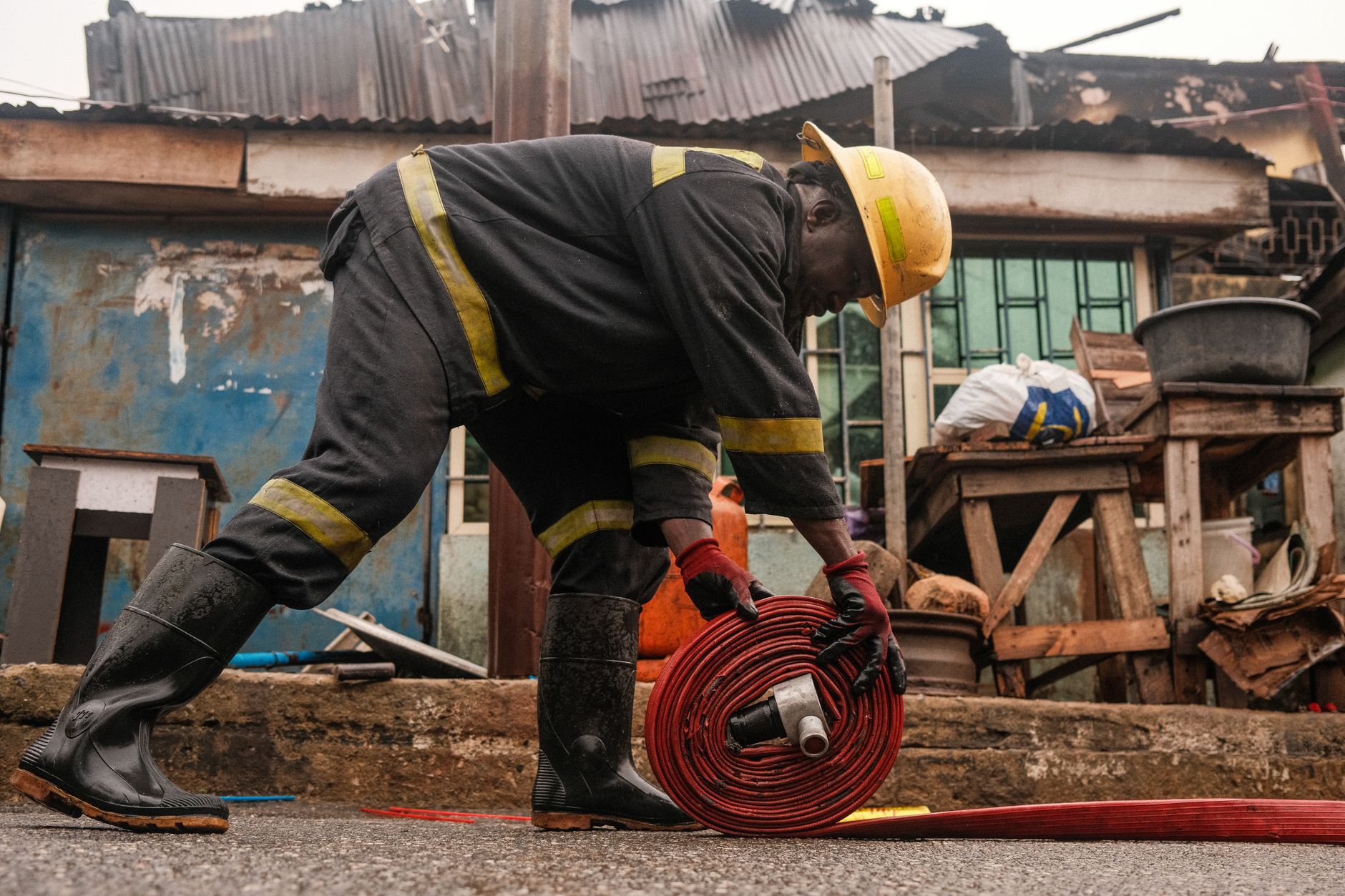 An African firefighter rolls up a fire hose in a Lagos neighborhood post-emergency.