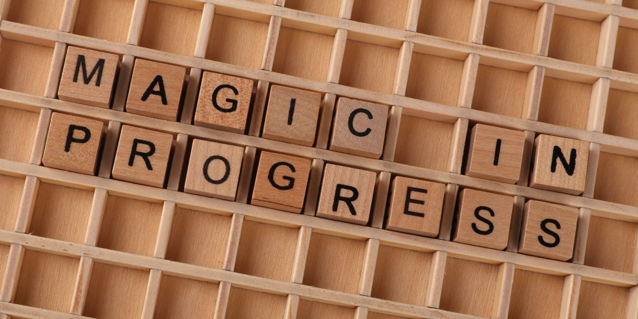 Wooden letter blocks arranged to spell 'Magic in Progress' on a grid.