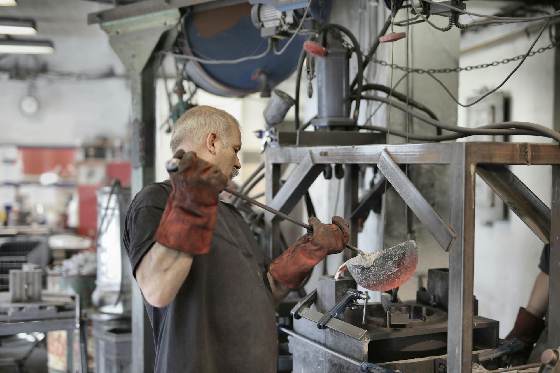 Side view of senior white hair worker in apron and heavy duty gloves melting detail from iron