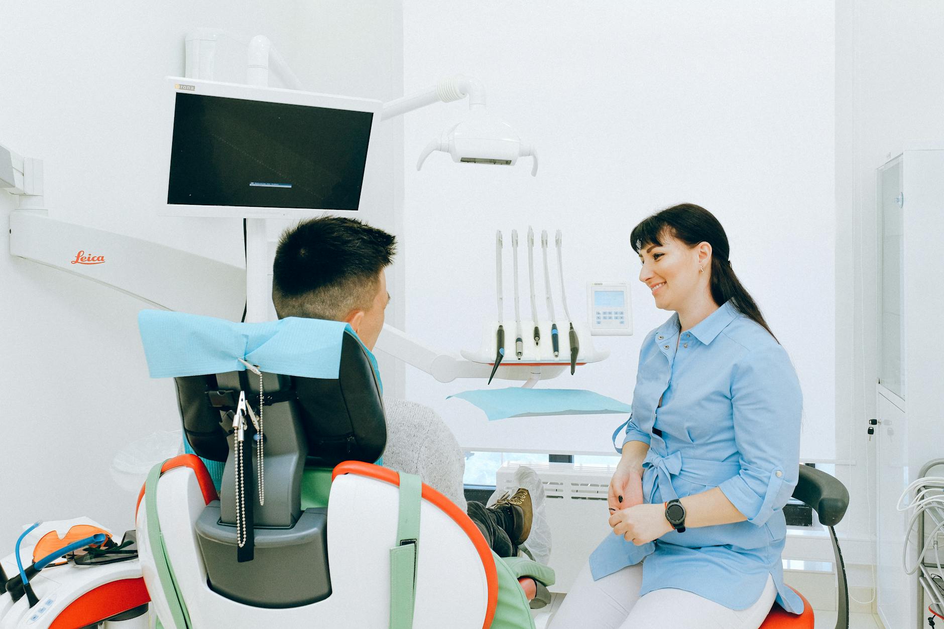 Content female dentist in uniform interacting with male patient sitting in shoe covers on dental chair during medical appointment in light doctor office