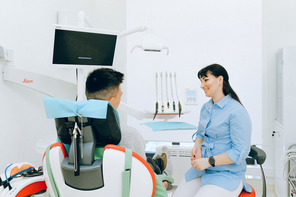 Free Cheerful stomatologist talking with patient sitting in dental chair Stock Photo