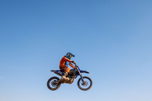 Free A motorcyclist in vibrant gear mid-air on a motocross bike with a clear blue sky backdrop. Stock Photo