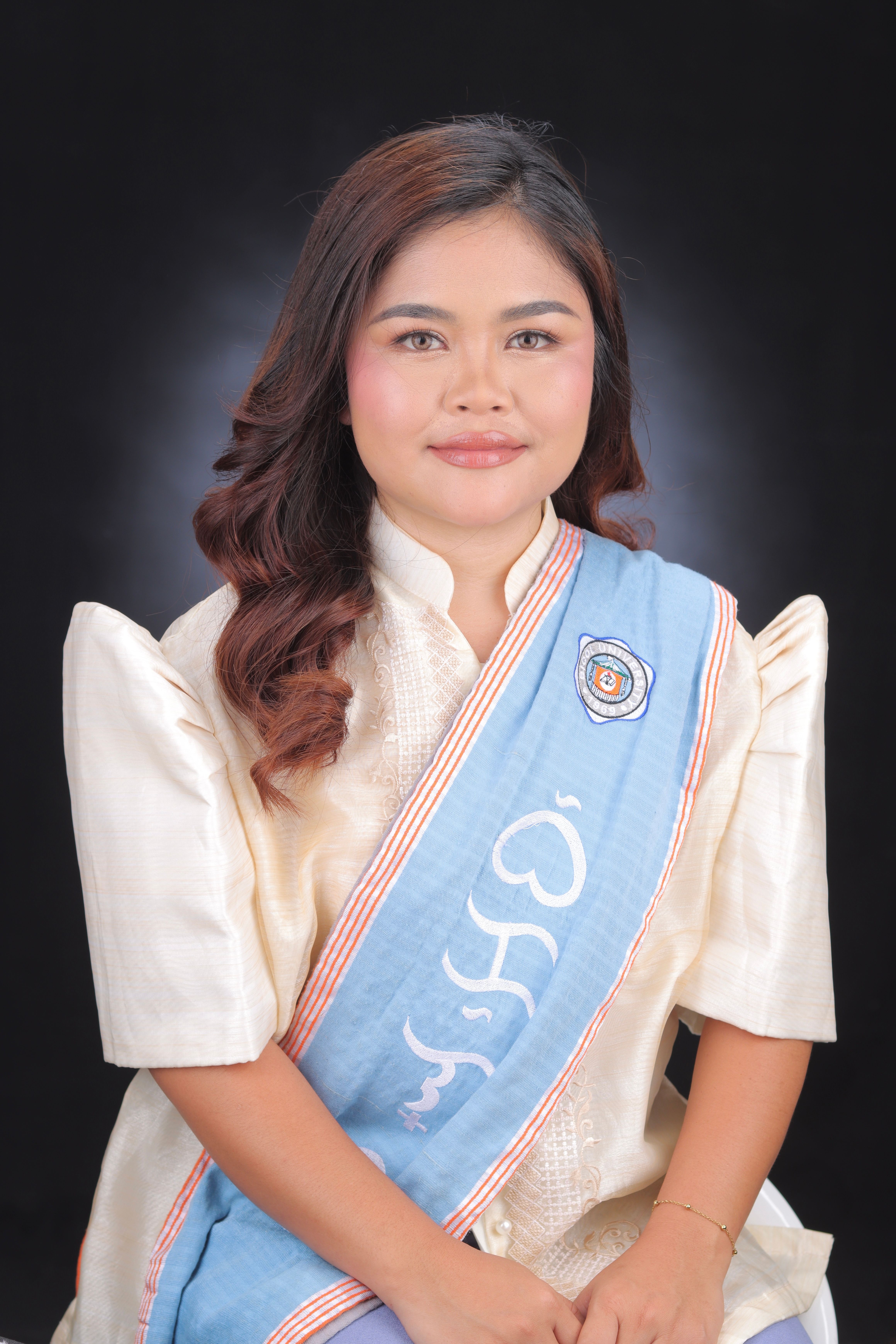 A young woman in traditional graduation attire sits smiling against a black background.