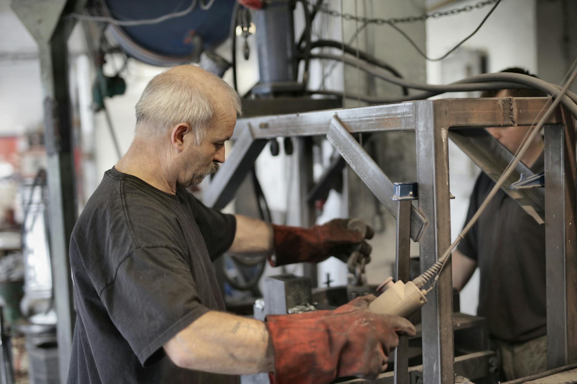 Side view of senior white hair craftsman in heavy duty gloves dealing with machine in workshop