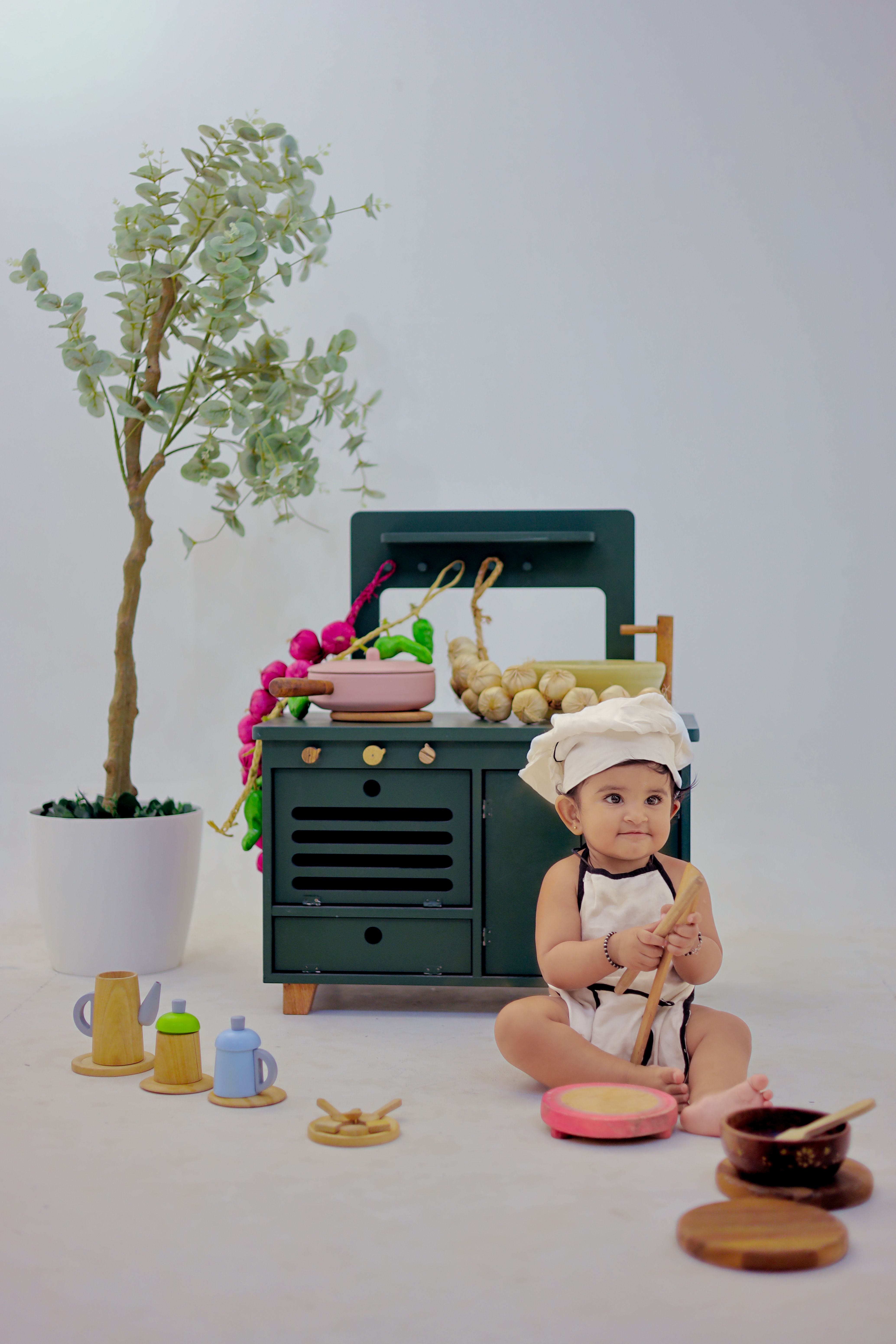 Charming baby dressed as a chef in a play kitchen with toy cookware.