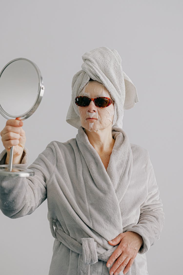 Stylish Woman In Home Clothes With Face Mask Looking In Mirror