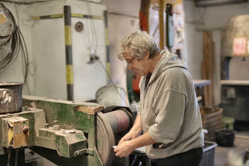 Senior white hair worker grinding detail on machine