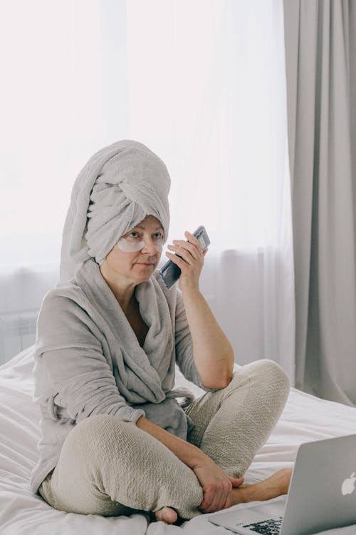 Free Woman in Gray Bathrobe Sitting on Bed Stock Photo