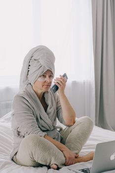 Adult woman in cozy bedroom with laptop and phone, remote work lifestyle.
