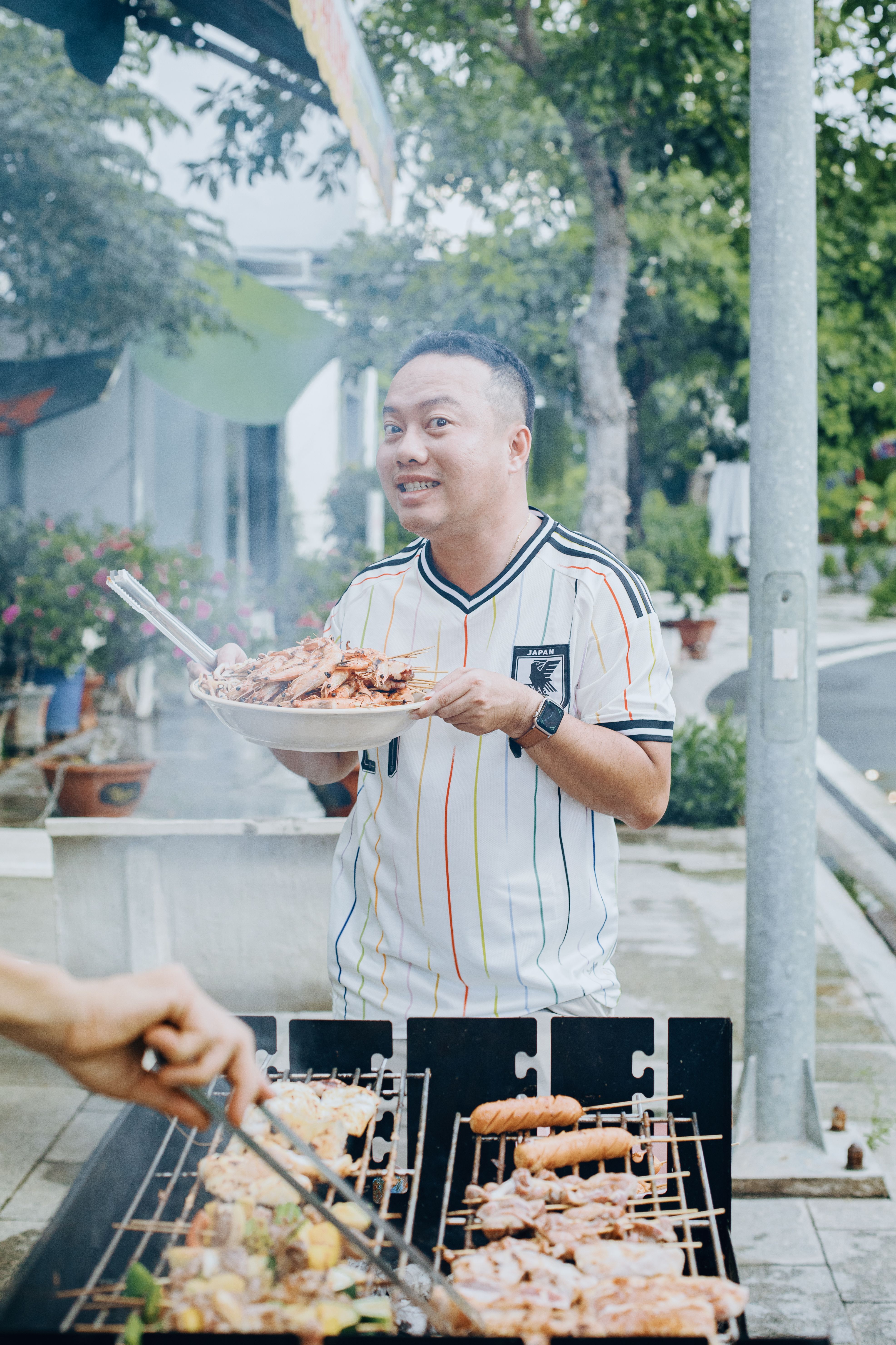 Man cooking meat on a grill during an outdoor barbecue party, showcasing lively social atmosphere.