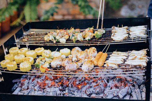 A variety of foods grilling over hot coals in an outdoor barbecue setup.