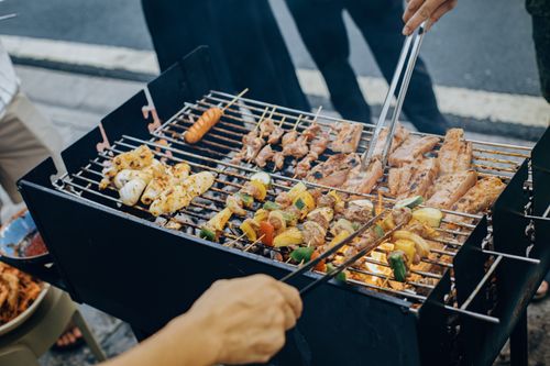 Free A lively street barbecue with various meats and vegetables grilling over charcoal. Stock Photo