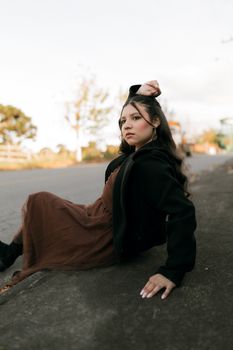 A young woman in a stylish outfit poses confidently on a suburban roadside.
