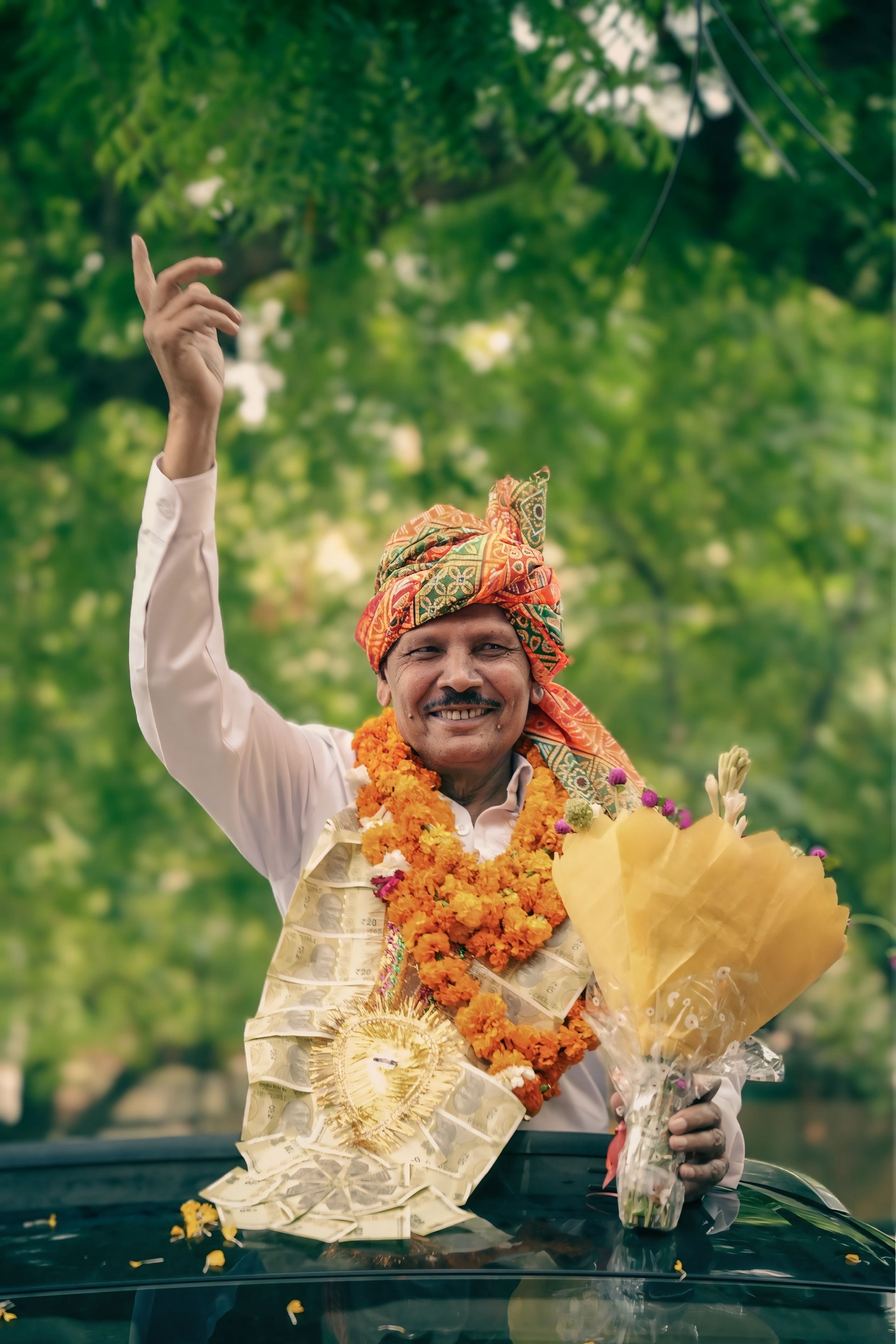 A happy man in traditional attire holding a bouquet, celebrating outdoors.
