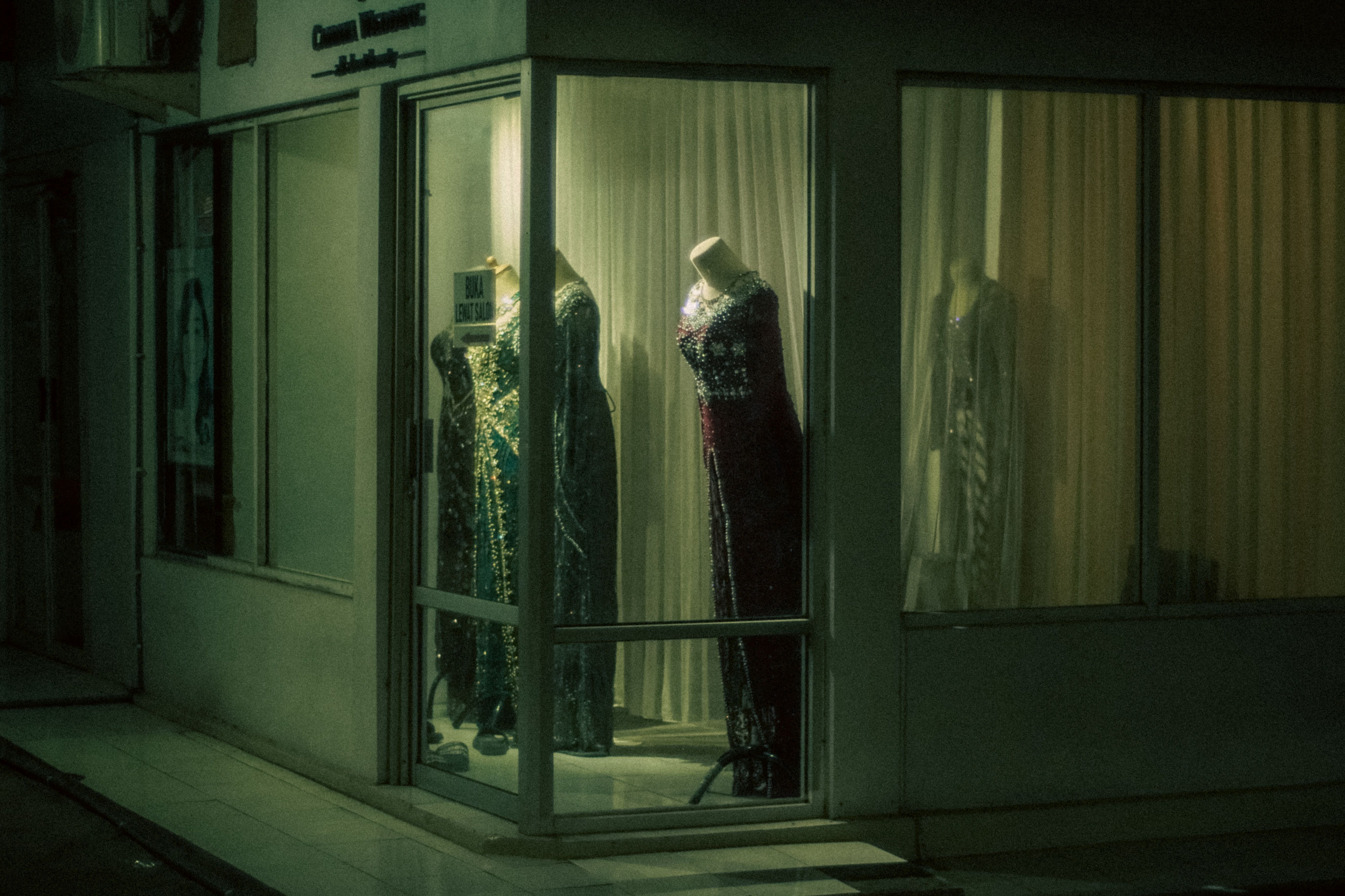 A lit shop window after dark, mannequins in evening dress and nobody yet at the door.