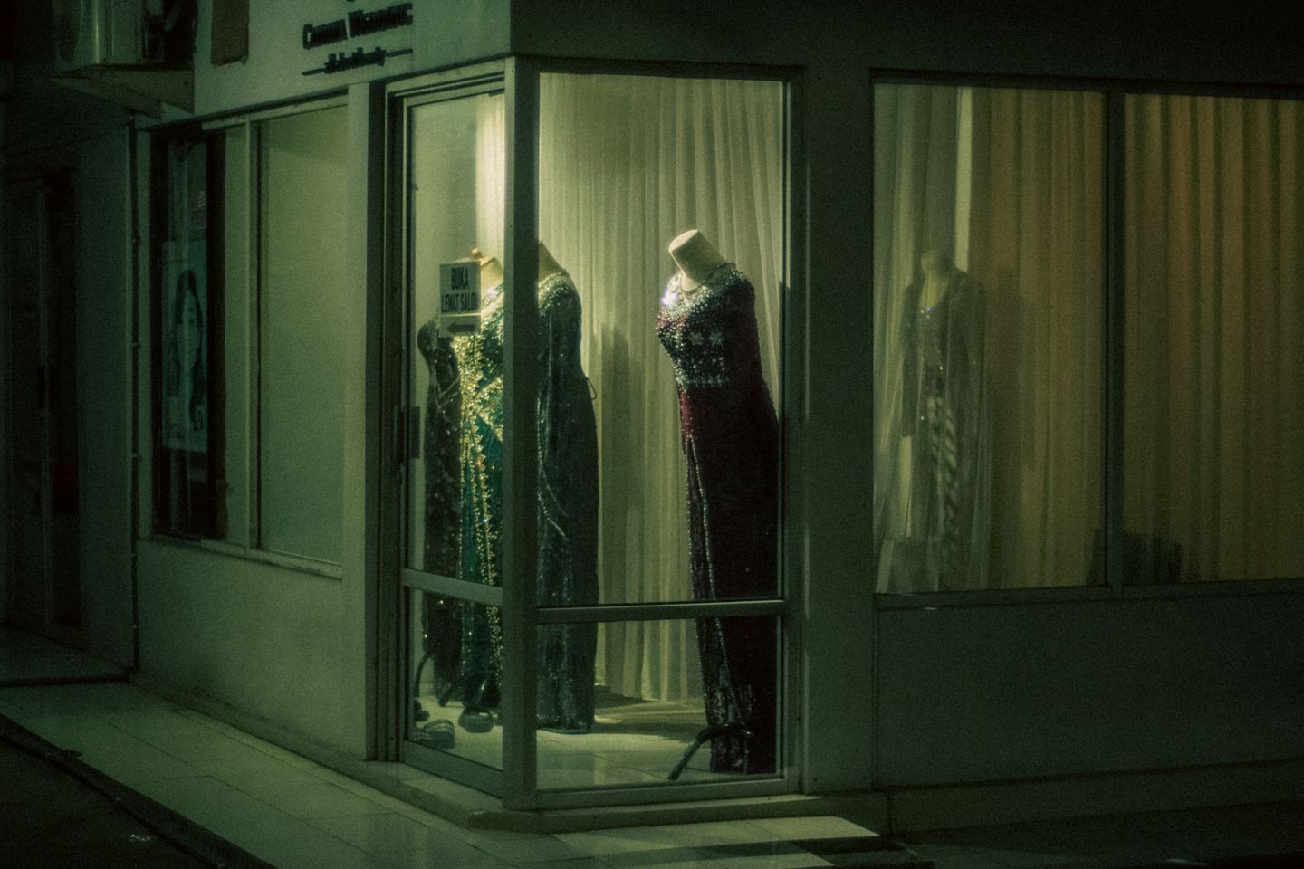 A lit shop window after dark, mannequins in evening dress and nobody yet at the door.