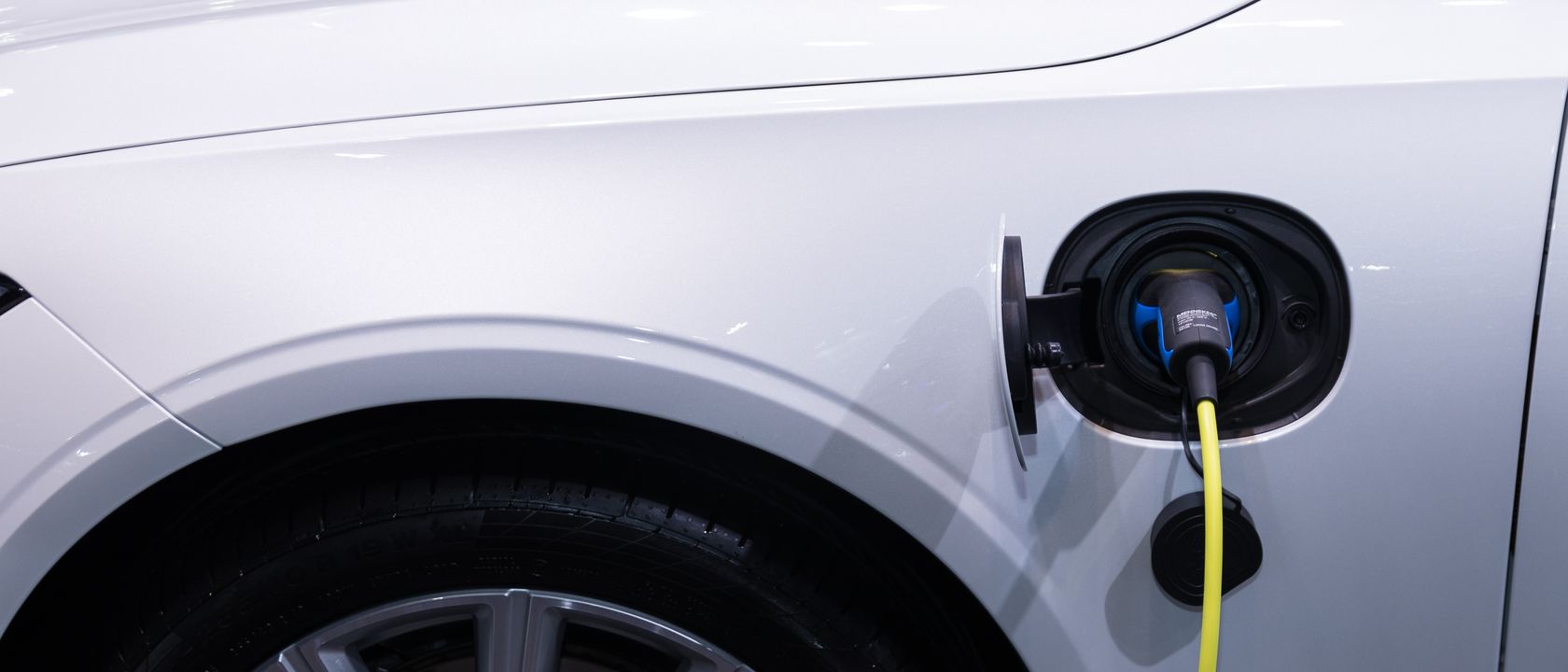 A white electric car is plugged in for charging, close-up view of the charging port.