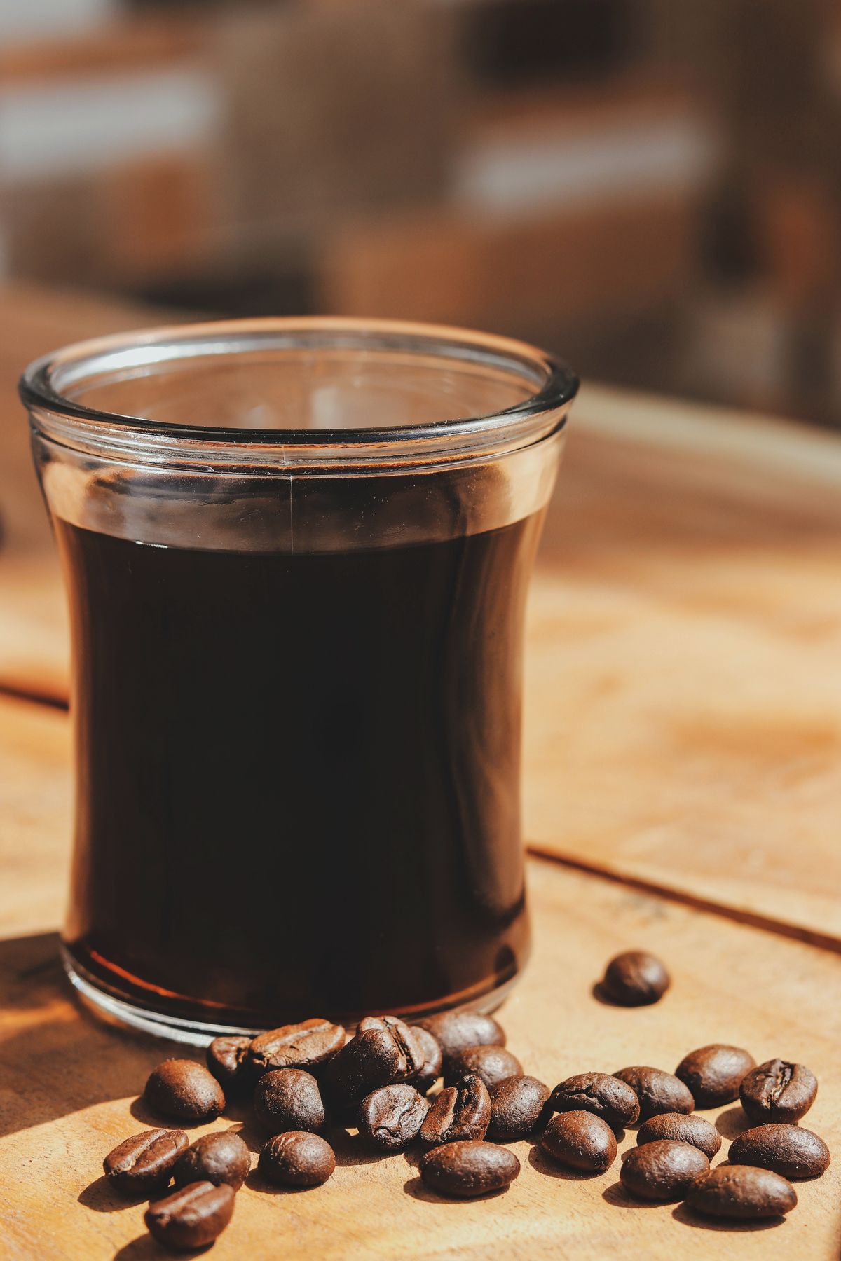 Pahar cu cafea neagra cu corp plin si boabe de cafea prajite langa el