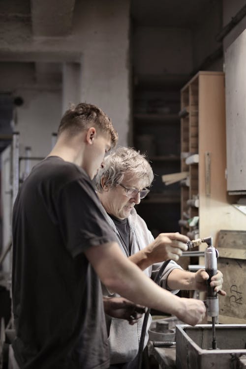 Apprentice helping master assembling detail in workshop