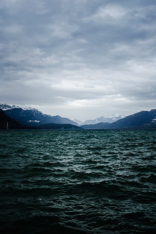 Free Body Of Water Near Mountain Under Cloudy Sky Stock Photo