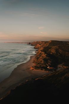 Dramatic cliffs and serene beach along Portugal's Algarve coast during sunset.