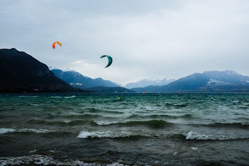Wavy ocean behind spectacular mountains and flying parachutes in evening