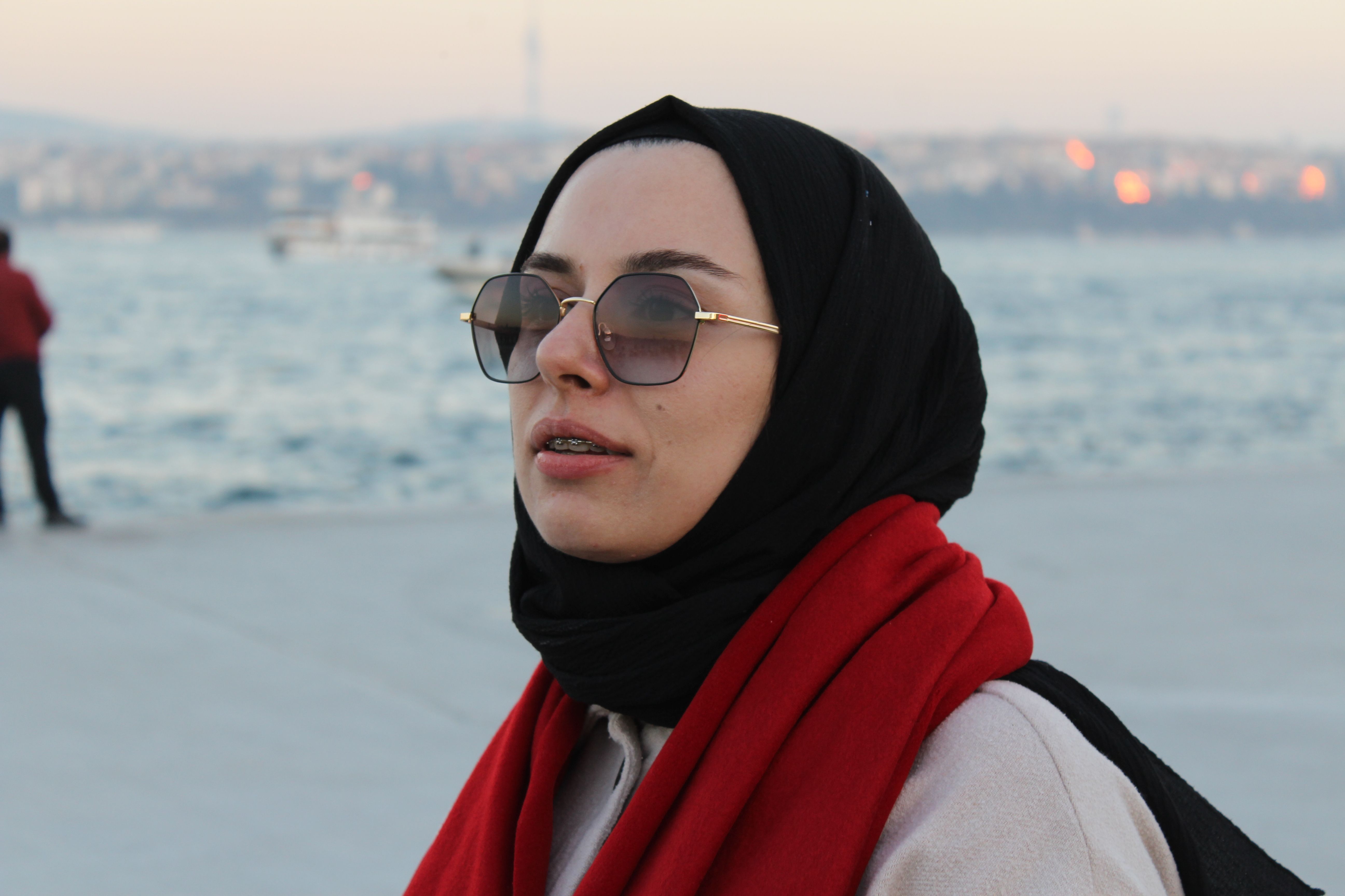 Woman with hijab and sunglasses by waterfront during sunset.