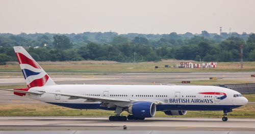 Free British Airways Boeing 777 airplane on airport runway with trees in the background. Stock Photo