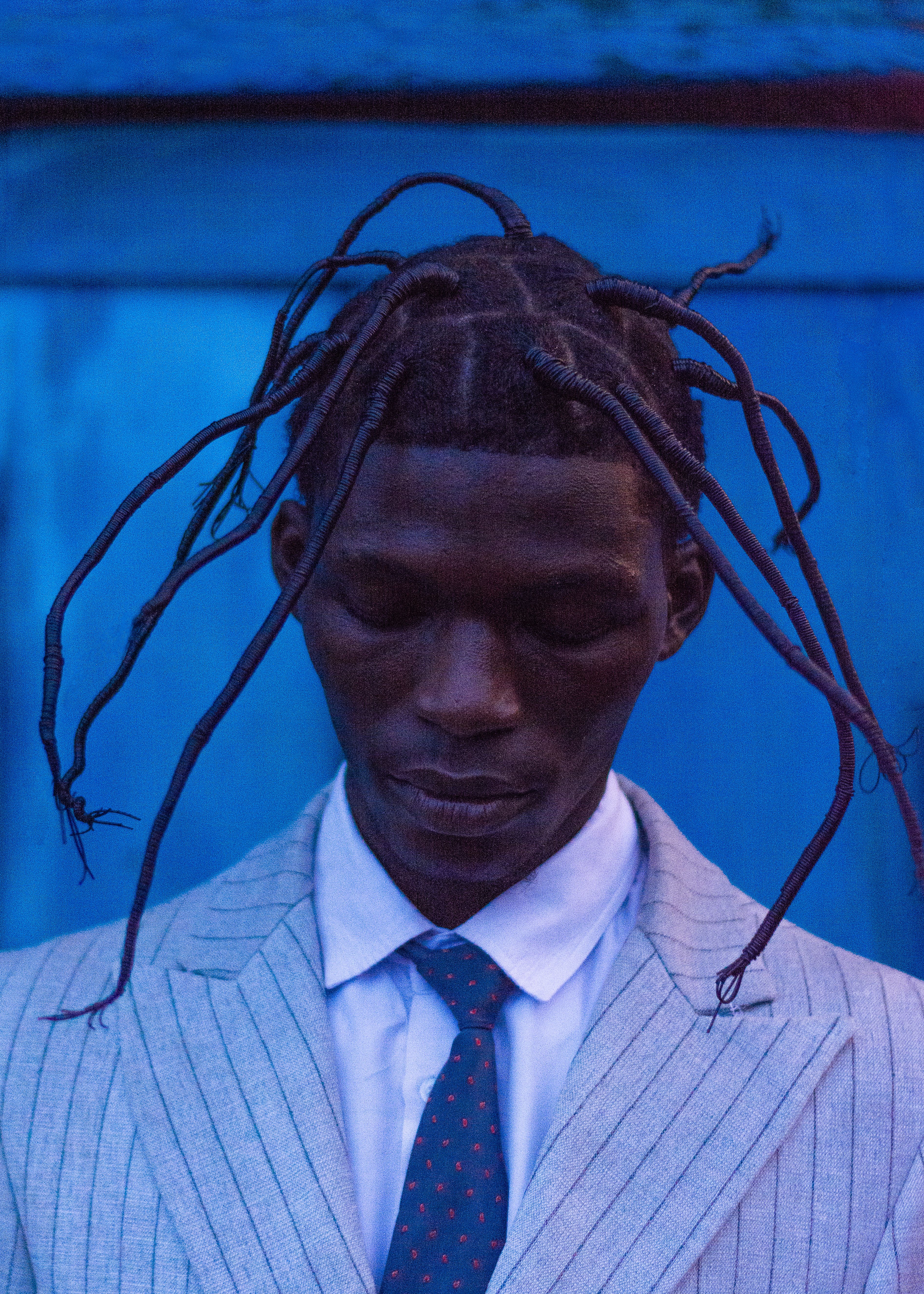 A portrait of a stylish person with unique braided hairstyle against a blue background.