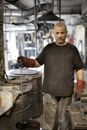 Elderly white hair craftsman in heavy duty gloves looking at camera while showing raw material in workshop