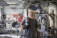 Pleased senior white hair craftsman in heavy duty gloves showing sandblaster and looking at camera