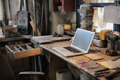 From above of modern laptop laying at table among different tools and equipment in workshop