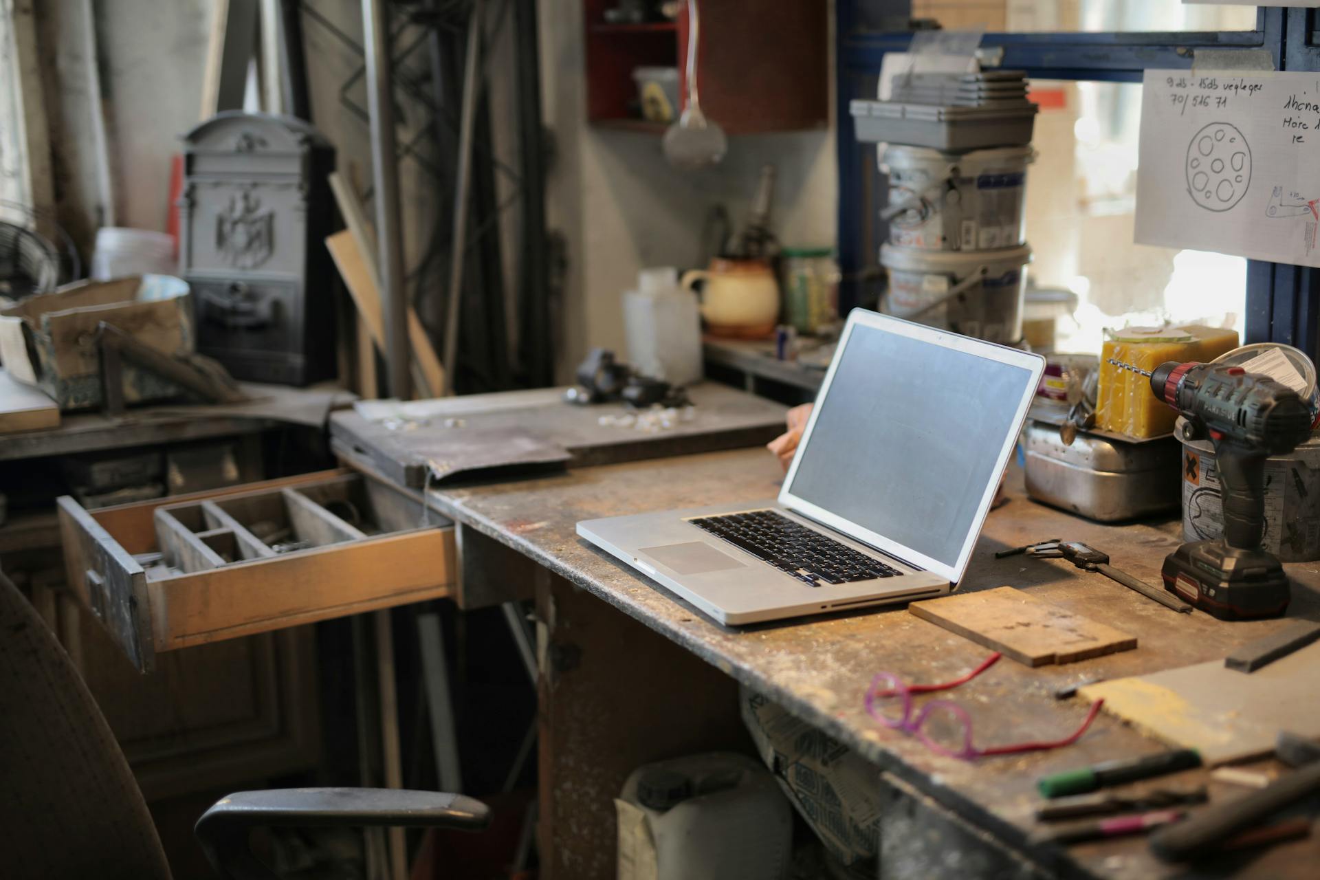 From above of modern laptop laying at table among different tools and equipment in workshop