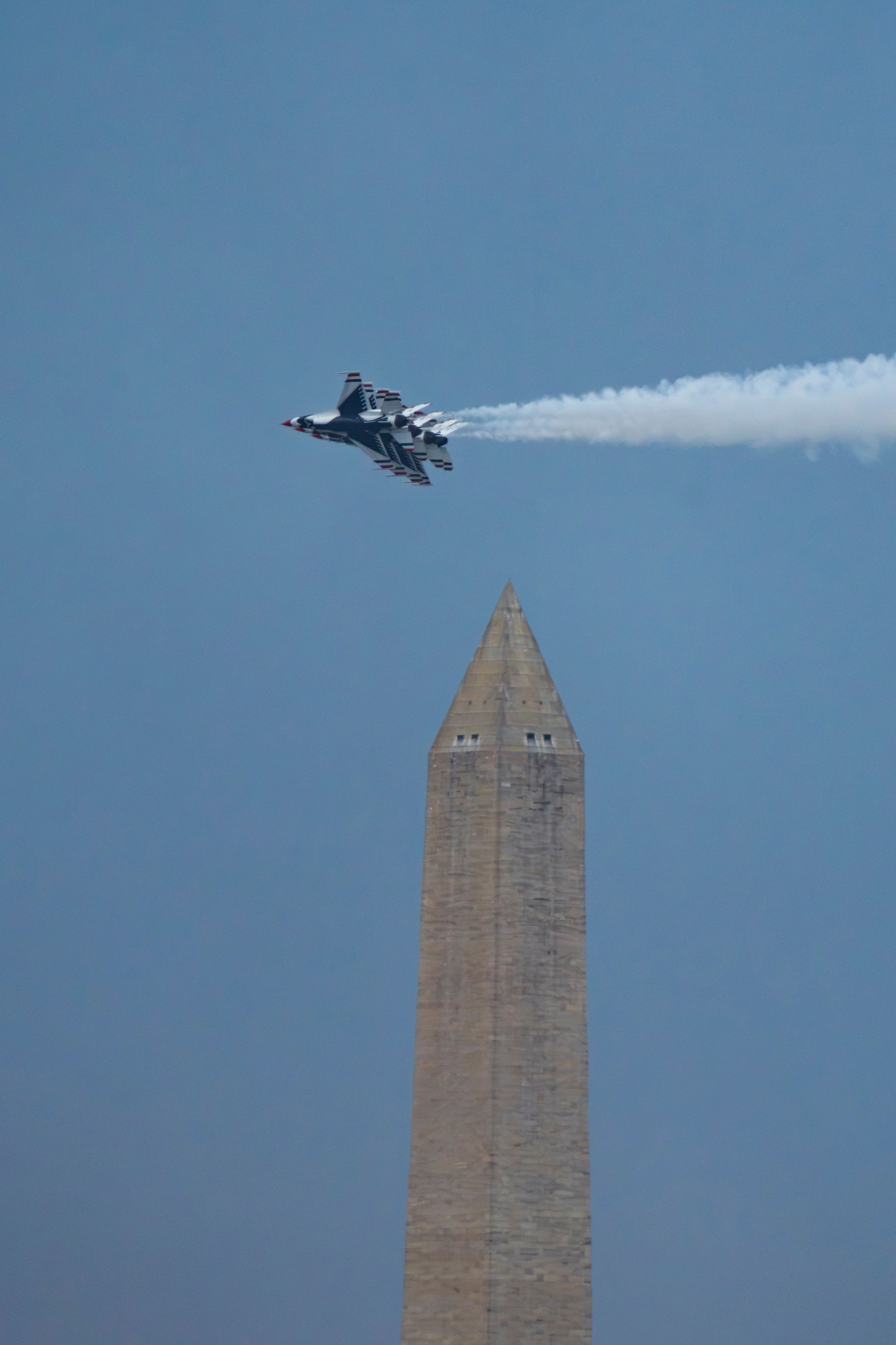 A Thunderbird jet flying over the iconic Washington Monument during the daytime.