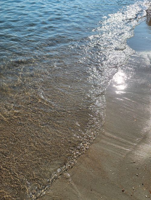 Free Calm waves gently lapping on a sandy beach with sunlight reflecting on the surface in Urla, İzmir. Stock Photo