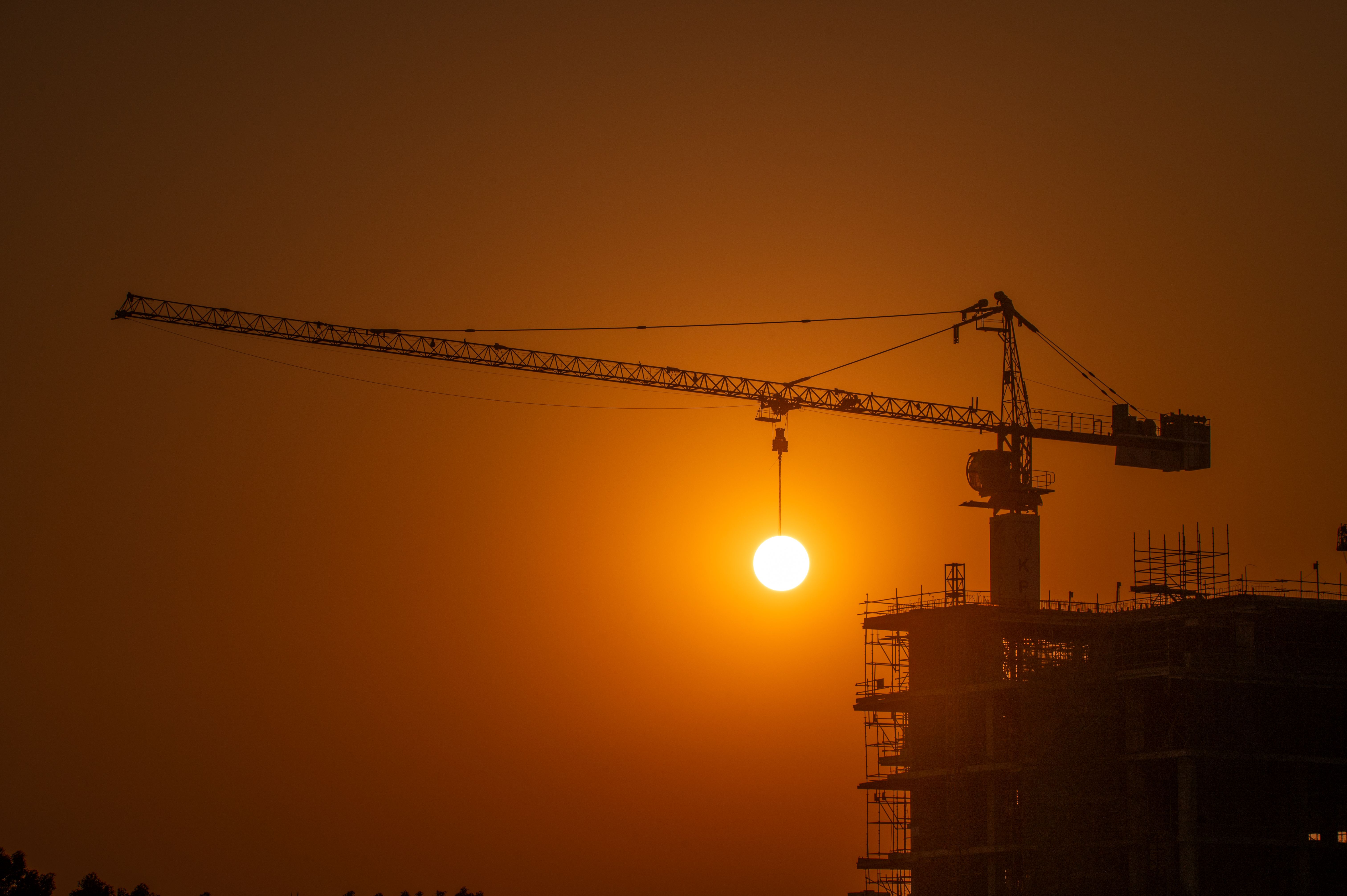 A construction crane silhouetted against the Dubai skyline at sunset