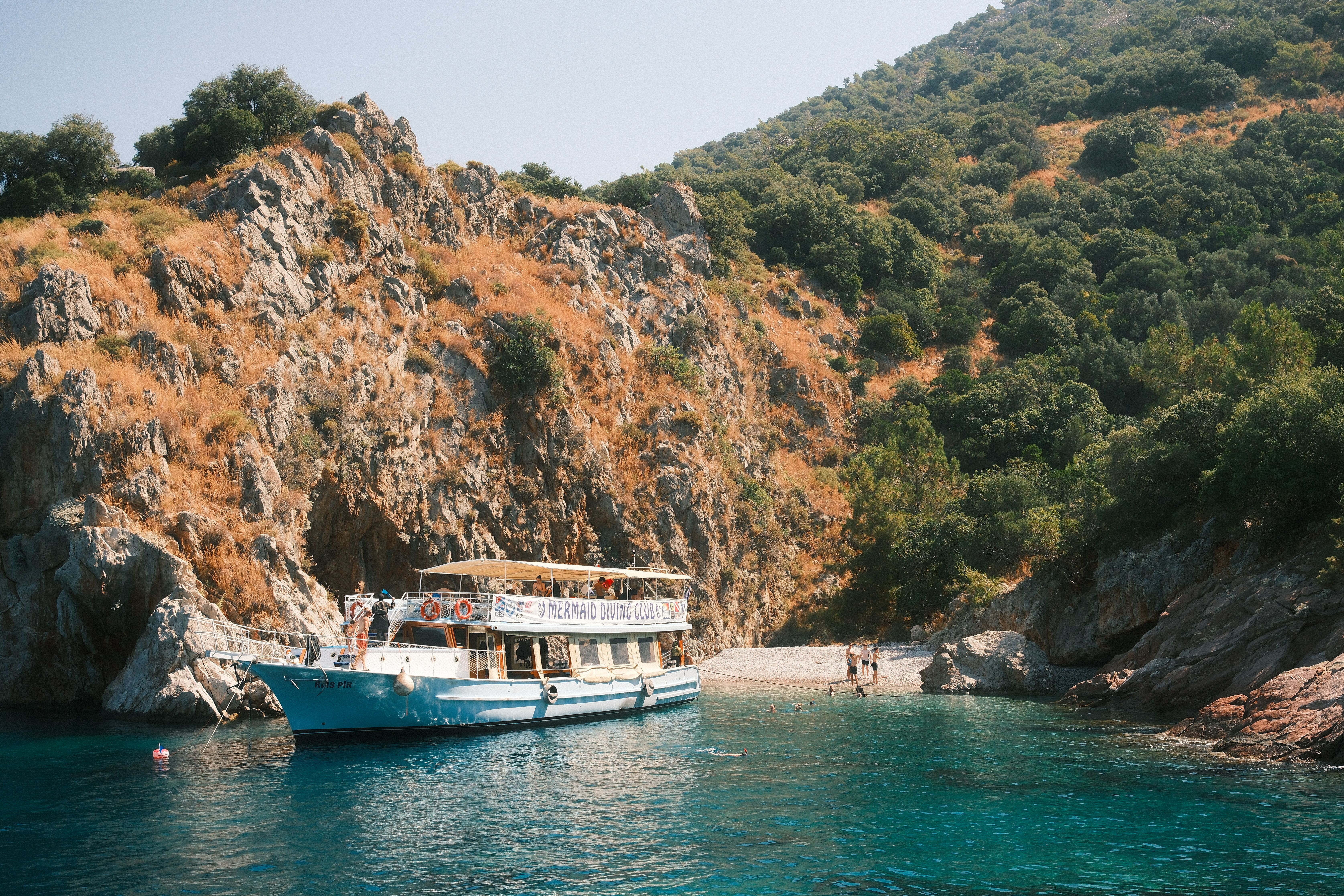 A tranquil coastal scene featuring a diving boat near rocky hillsides and clear blue waters.