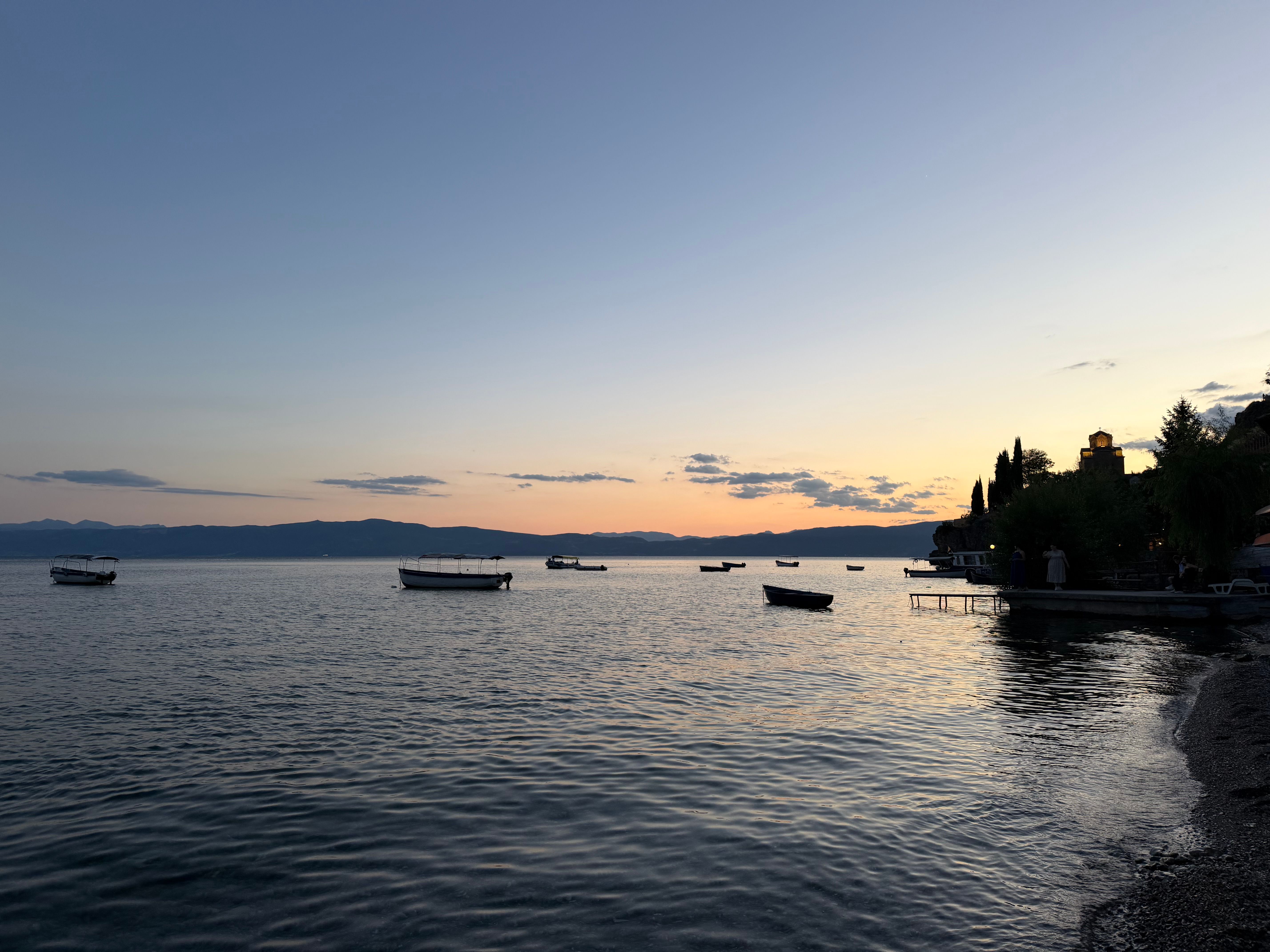 A tranquil sunset view over Lake Ohrid with boats floating peacefully near the shore.