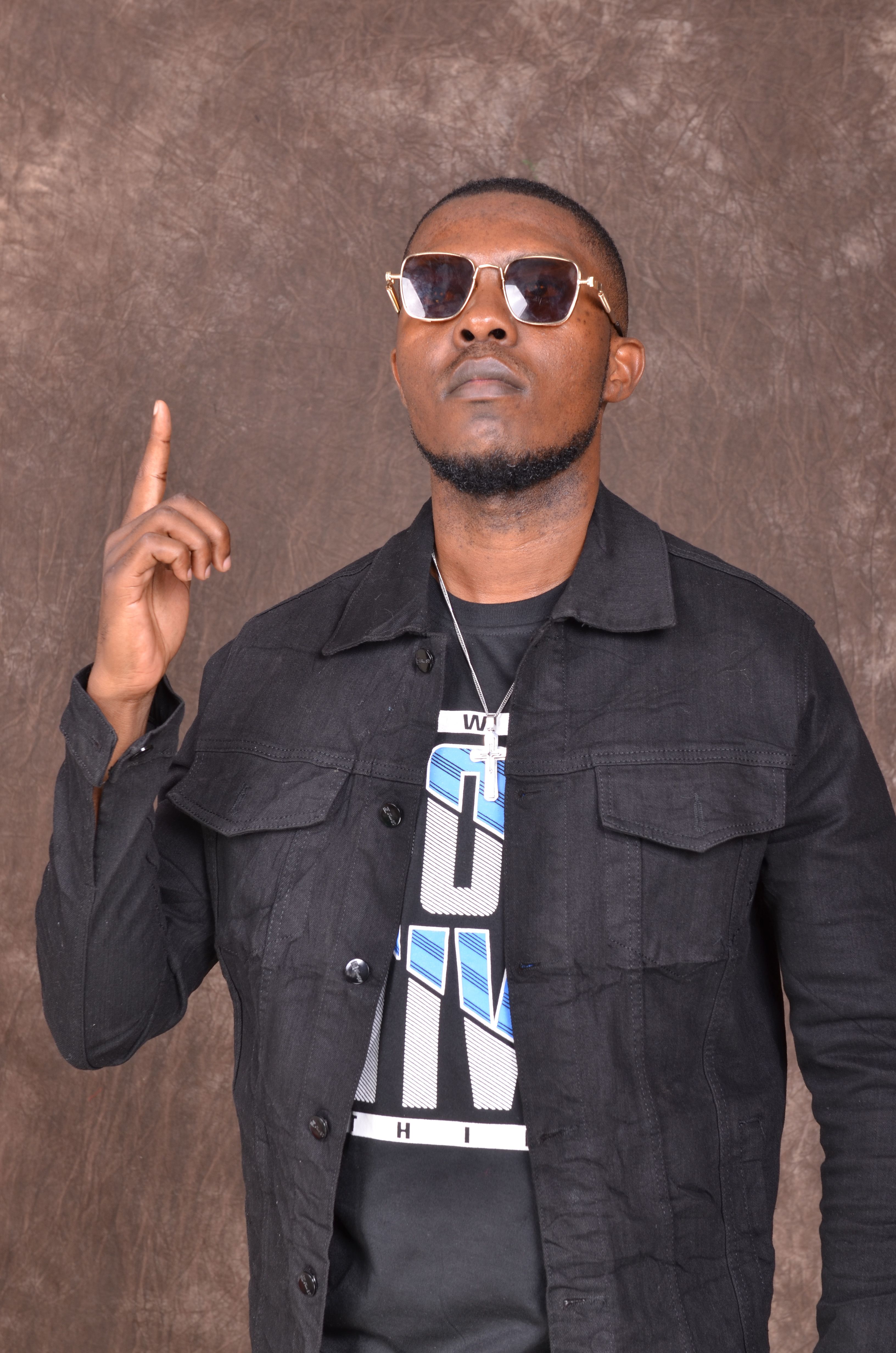 Stylish man in sunglasses and black jacket pointing upwards with confidence.